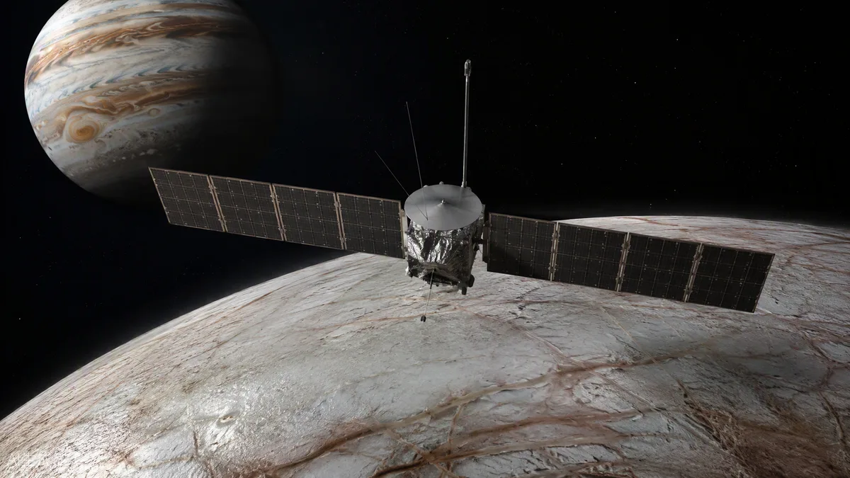 Sonde spatiale aux grands panneaux solaires survolant la surface glacée et craquelée d’Europe, Jupiter en arrière-plan